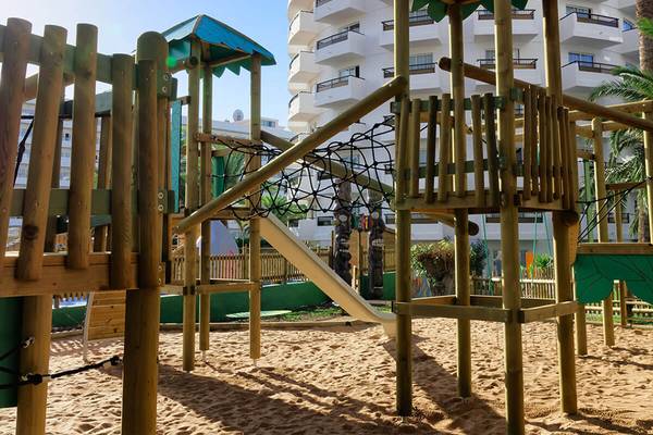 Spielplatz vor dem Servatur Waikiki Hotel mit Holzspielgeräten und einer Rutsche.