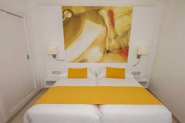Doppelzimmer im Servatur Waikiki Hotel mit zwei Betten, gelben Kissen und einem Gemälde an der Wand.