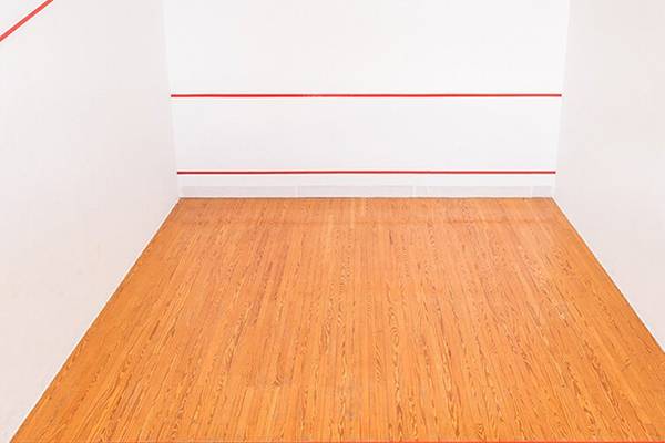 Leere Squashhalle mit roten Linien auf weißen Wänden und einem hölzernen Boden.