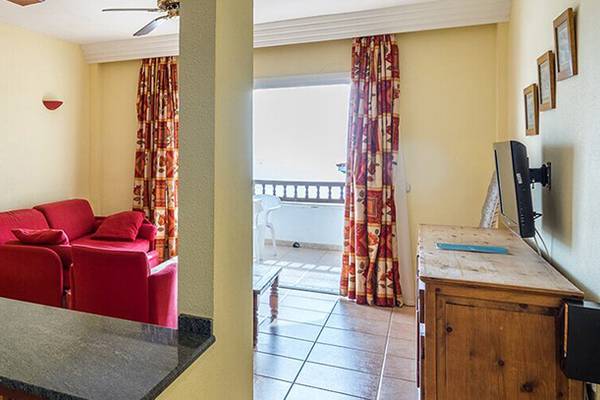 Wohnbereich des Bluesea Callao Garden Hotels mit Küchenzeile, rotem Sofa und Fernseher.