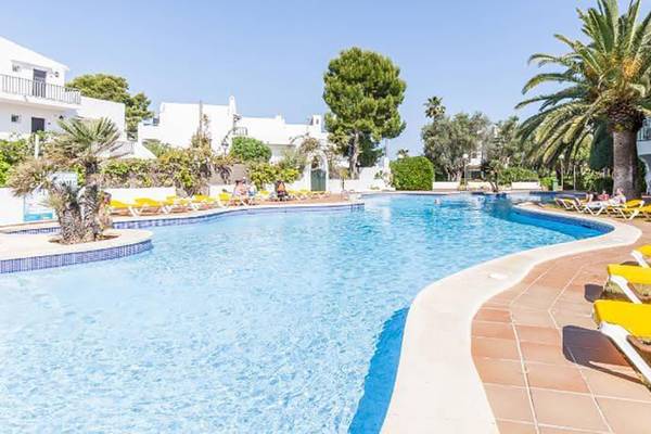 Ein Swimmingpool mit gelben Sonnenliegen umgeben von Palmen und Gebäuden des Hotels BLUESEA Callao Garden.