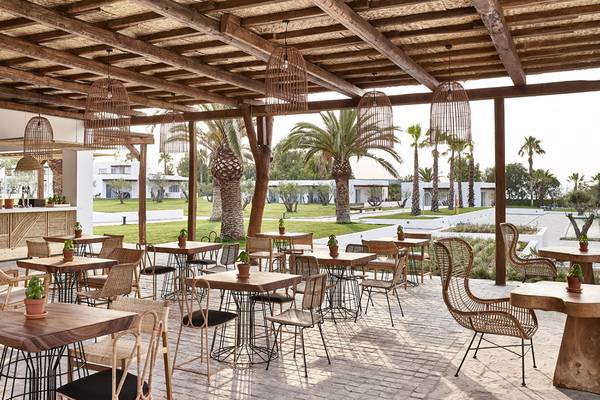 Außenterrasse des Grecotel Casa Marron Hotels mit Tischen, Stühlen und Palmen im Hintergrund.