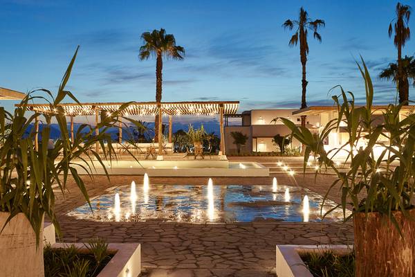 Abendansicht des Grecotel Casa Marron Gartens mit beleuchtetem Wasserbrunnen und Pflanzen.