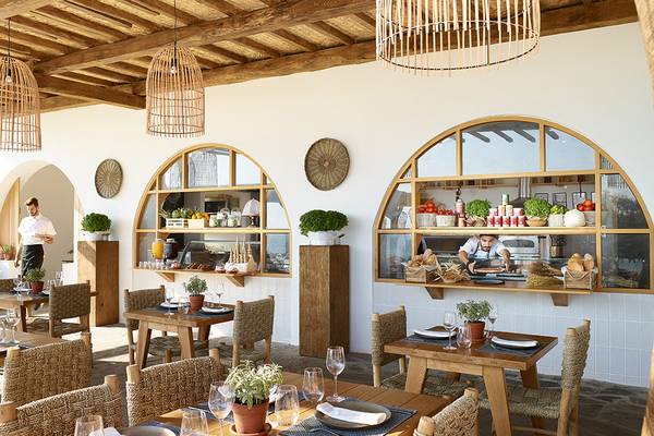 Innenansicht des Grecotel Casa Marron Restaurants mit Holztischen, Stühlen und Pflanzen.