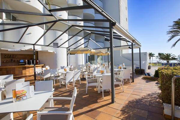 Außenterrasse des Hipotels Hipocampo Playa Hotel mit weißen Tischen und Stühlen unter Sonnenschirmen.