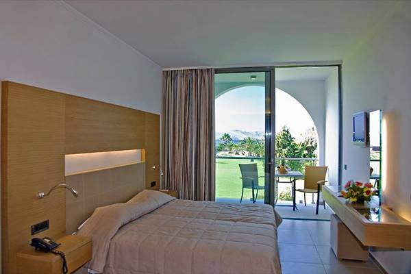 Zimmer im Caravia Beach Hotel mit Aussicht auf den Strand, mit einem Bett, einem Tisch, Stühlen und einem Balkon.