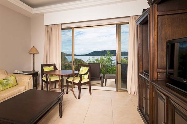 Hotelzimmer mit Seeblick im Occidental Papagayo mit Wohnzimmer, Tisch, Stühlen und Fernseher.