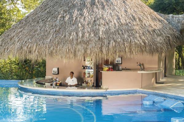 Ein Hotel mit einer Bar unter einem Palmendach neben einem Swimmingpool.