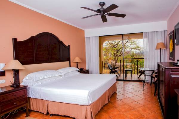 Ein komfortables Hotelzimmer im Occidental Papagayo mit einem großen Bett, Balkon und Blick auf die Natur.