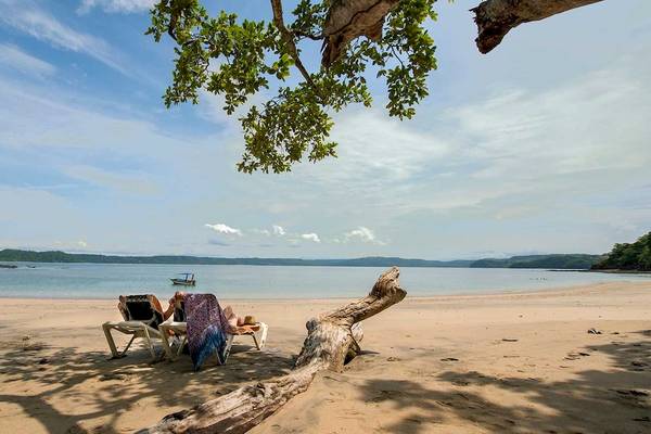 Zwei Gäste entspannen auf Liegen am Strand des Occidental Papagayo Hotels.