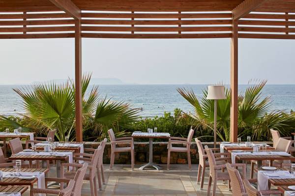 Außenterrasse des The Island Hotel auf Kreta mit Blick auf das Meer und üppigem Grün.
