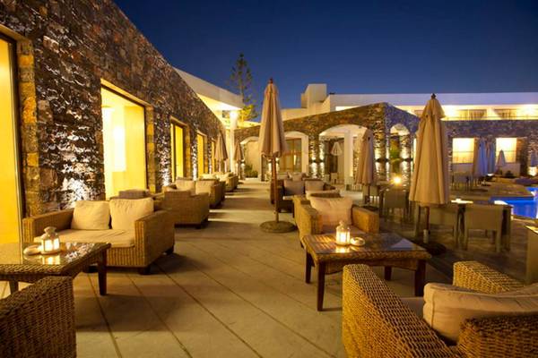 Abendterrasse des Island Hotels auf Kreta mit steinernen Wänden, Rattanmöbeln und blau beleuchtetem Pool.