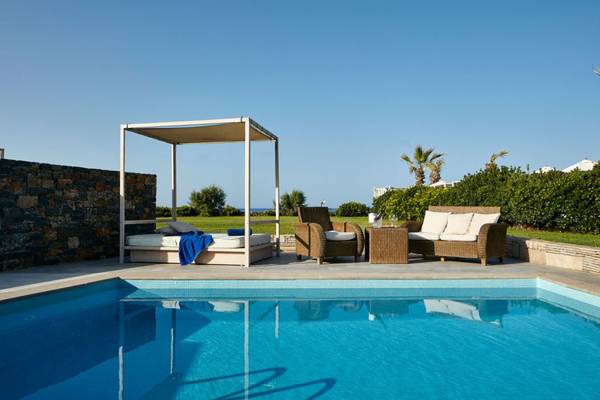 Der Island Hotel auf Kreta zeigt eine Poolseite mit einem Bett und Sitzen.