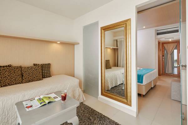 Schlafzimmer im Insel Hotel Kreta mit Bett, Nachttisch, Spiegel und offenem Fenster.