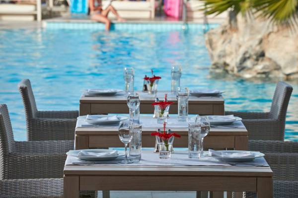 Tische am Pool im Island Hotel Kreta mit Wassergläsern und roten Blumen.