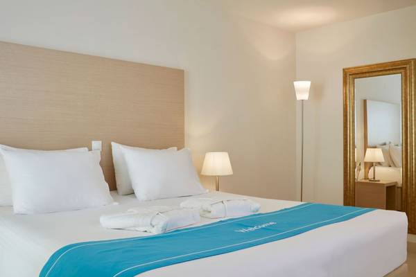 Schlafzimmer im Island Hotel auf Kreta mit einem Bett, Kissen, Decken, und Nachttischlampen.