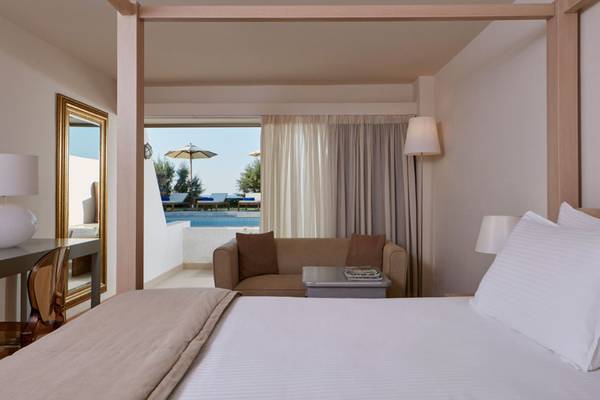 Schlafzimmer im Insel Hotel Kreta mit Sofa, Tisch, Spiegel und Poolblick.