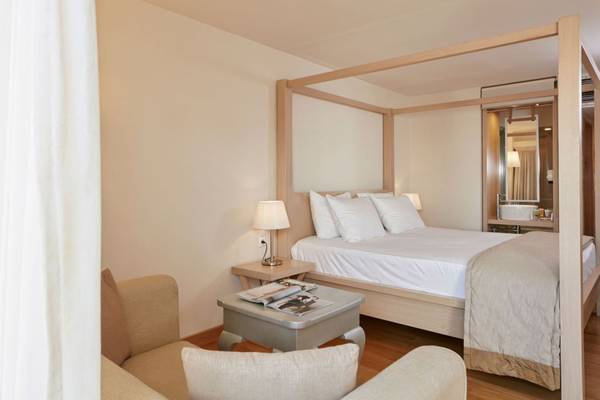 Schlafzimmer im Island Hotel auf Kreta mit Himmelbett, Nachttisch und Sessel.