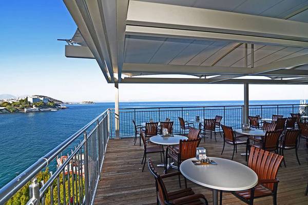 Hotelterrasse mit Blick auf das Meer, umgeben von vielen runden Tischen und Stühlen.