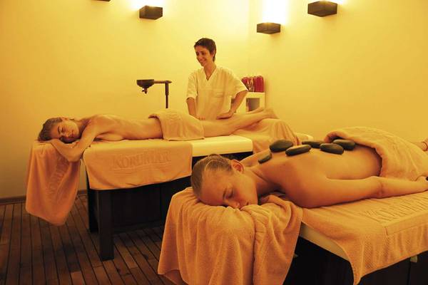Massagebehandlung im KoruMar Hotel De Luxe mit zwei Frauen auf Liegen und einer Therapeutin.