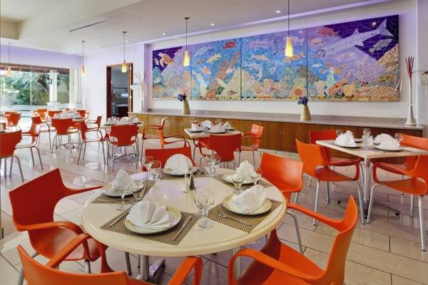 Innenansicht des Restaurants im Holiday Inn Resort Aruba mit orangen Stühlen und Tischen, einer großen Wandmalerei und einer Theke.