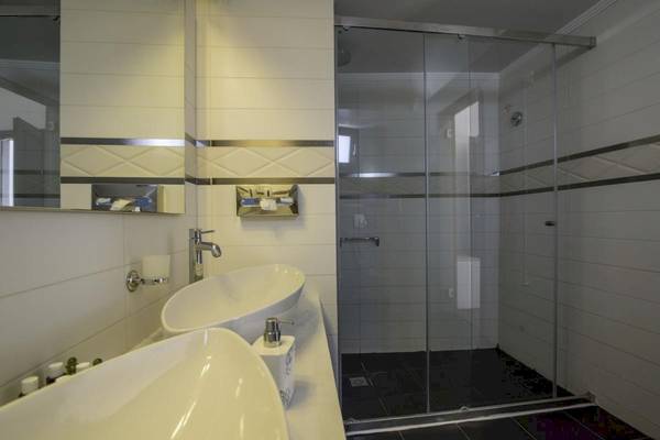 Badezimmer des La Mer Deluxe Hotel & Spa mit zwei Waschbecken, Glasdusche und Spiegel.