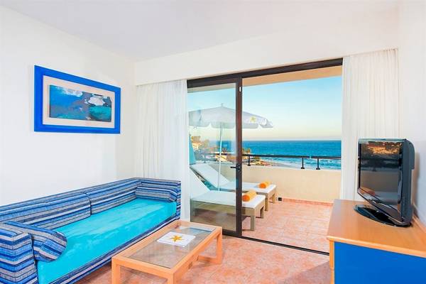 Balkon mit Meerblick im Iberostar Playa Gaviotas Hotel, mit Fernseher, Couch, Tisch und Sonnenschirmen.