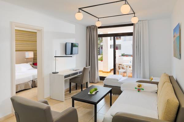 Innenansicht des H10 Suites Lanzarote Gardens Zimmers mit Schreibtisch, Sofa und zwei Betten.