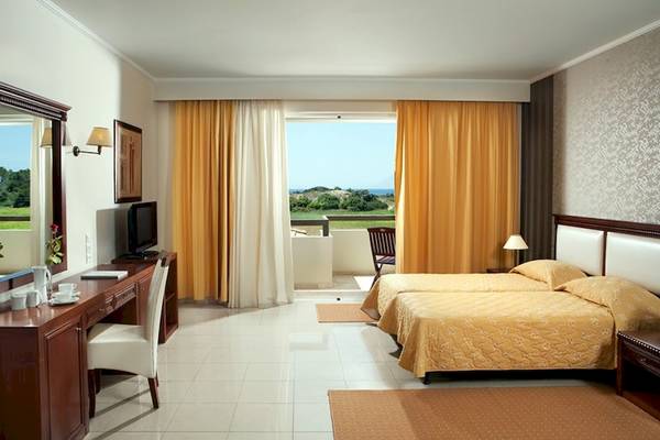 Doppelzimmer mit Balkon im Olympia Golden Beach Resort, mit zwei Betten, Schreibtisch und Fernseher.