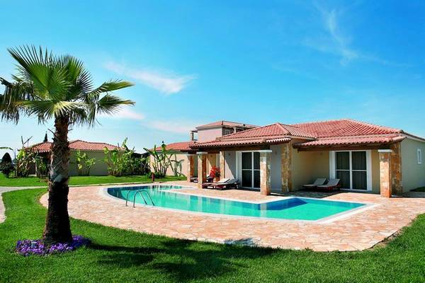 Villa des Olympia Golden Beach Resorts mit Swimmingpool, Palme und Liegestühlen im Freien