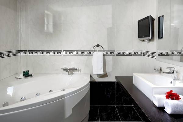 Badezimmer im Olympia Golden Beach Resort mit Badewanne, Waschbecken und Fernseher an der Wand.