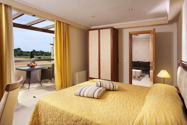 Hotelzimmer im Olympia Golden Beach Resort mit Balkon, Tisch, Stühle, Bett, Kleiderschrank, Lampe und Wohnbereich