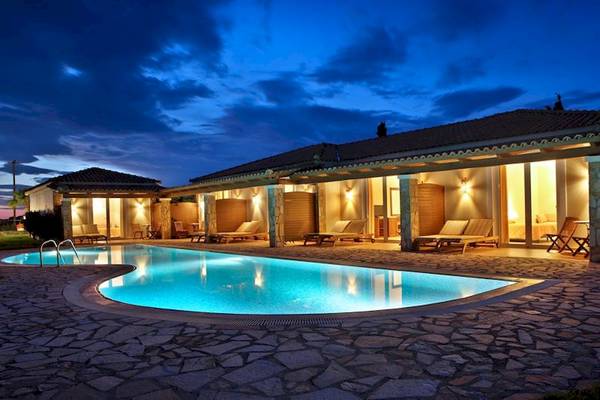 Nachtansicht des Olympia Golden Beach Resorts mit beleuchtetem Swimmingpool und Loungebereichen.