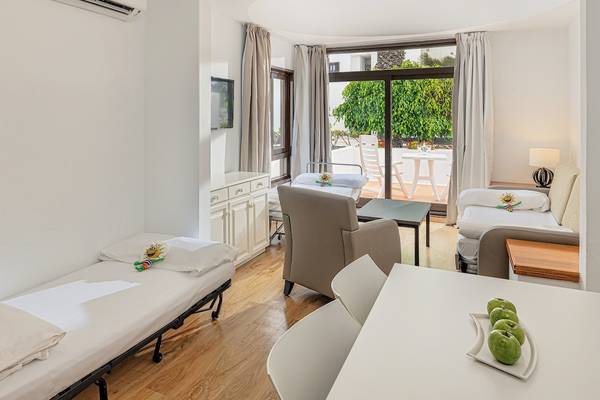 Innenansicht eines Schlafzimmers im H10 Suites Lanzarote Gardens mit zwei Betten, einem Tisch und einem Sessel.