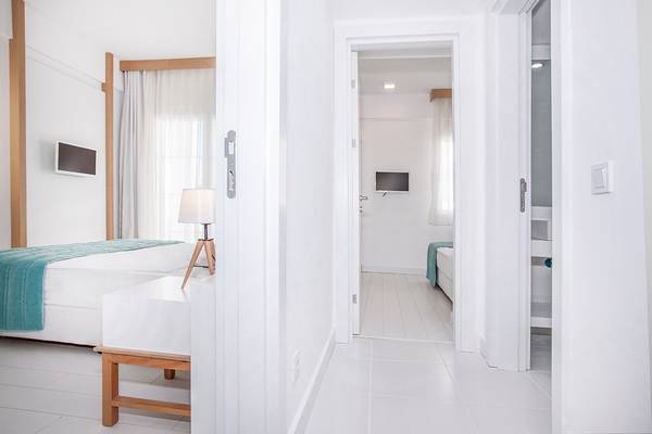 Innenansicht eines Zimmers im Labranda TMT Bodrum Hotel mit weißem Interieur, Bett, Tisch und Fernseher.