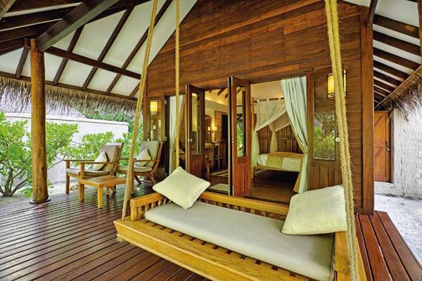 Medhufushi Island Resort Holzbungalow mit Terrasse, Hängeschaukel und Innenansicht eines Schlafzimmers.