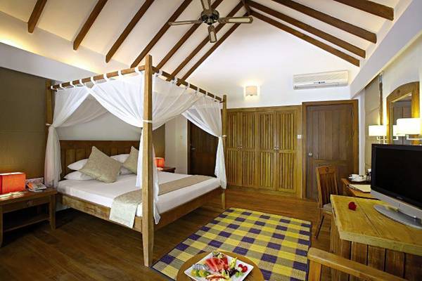 Schlafzimmer im Medhufushi Island Resort mit einem Baldachinbett, einem Fernseher, einem Schreibtisch und einem gemusterten Teppich.