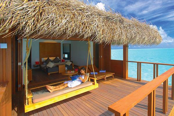 Gast im Medhufushi Island Resort genießt Blick aufs Meer von der Hängematte im Überwasser-Bungalow
