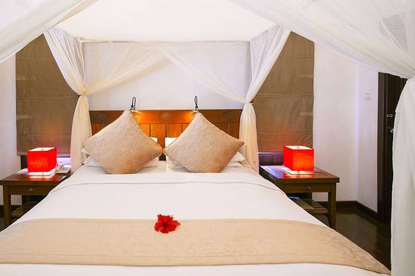 Ein geräumiges Hotelzimmer im Medhufushi Island Resort mit einem Bett, zwei Kissen, roten Nachttischlampen und einer roten Rose auf dem Bett.