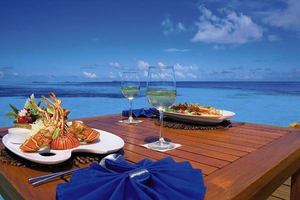 Ein Tisch am Strand mit zwei Gläsern Wein und Tellern mit Essen, Blick aufs Meer