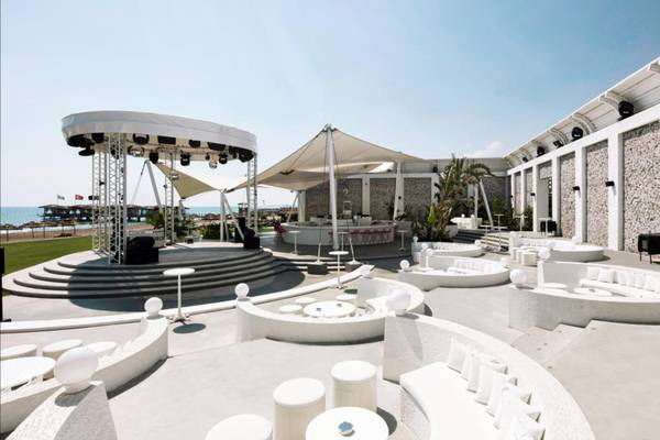 Außenbereich des Maxx Royal Belek Golf Resort mit weißen Möbeln und einer Bühne.