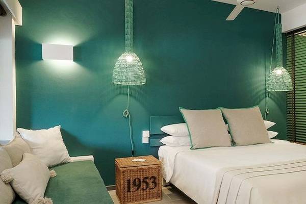 Schlafzimmer im Recif Attitude Hotel mit türkisgrünen Wänden, weißen Bettwäsche und grünen Lampen.