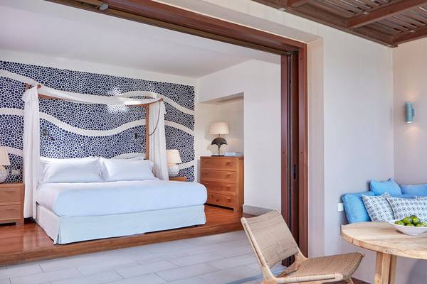 Innenansicht eines Schlafzimmers im Blue Palace Resort & Spa mit blauen und weißen Wandmustern, Bett, Nachttischen und einem offenen Balkon.