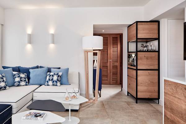 Modernes Wohnzimmer im Blue Palace Resort & Spa mit weißen Möbeln, blauen Kissen und einer Holzlampe.
