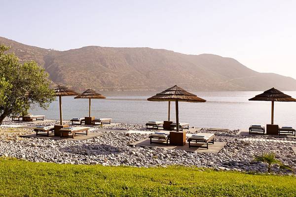 Strand des Blue Palace Resort & Spa mit Liegen, Sonnenschirmen und Blick auf die Berge.