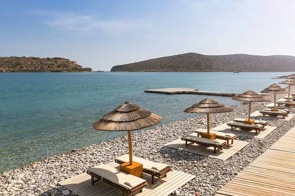 Außenbereich des Blue Palace Resorts mit Strand, Liegen und Sonnenschirmen, Blick auf das Meer und Berge.