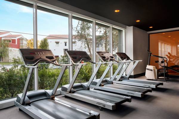 Fitnessraum im IC Santai Family Resort mit mehreren Laufbändern neben großen Fenstern.