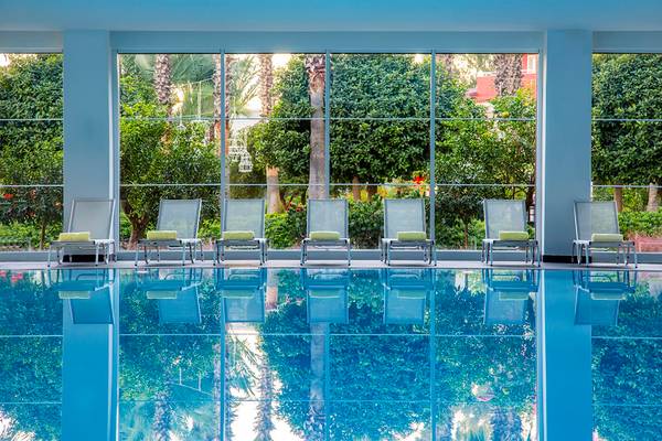 Pool mit Lounge-Stühlen im IC Santai Family Resort, umgeben von Pflanzen und Bäumen.