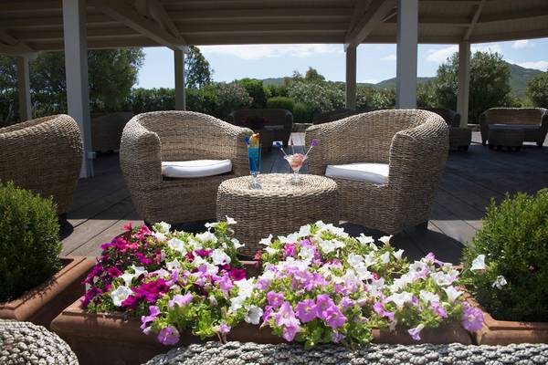 Terrasse des Abi d'Oru Beach Hotel mit Korbsofas, Blumen und Getränken.