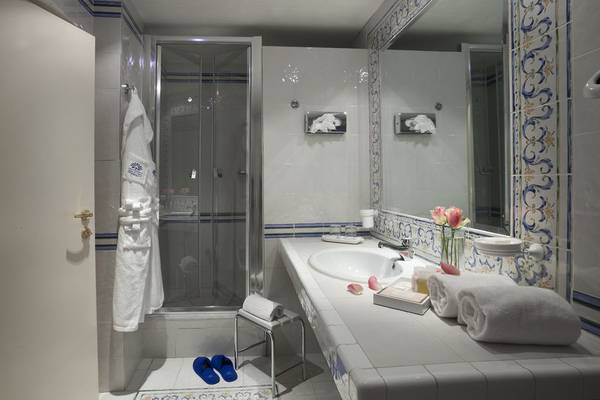 Badezimmer im Abi d'Oru Beach Hotel & Spa mit Dusche, Waschbecken und blauen Badeschuhen.